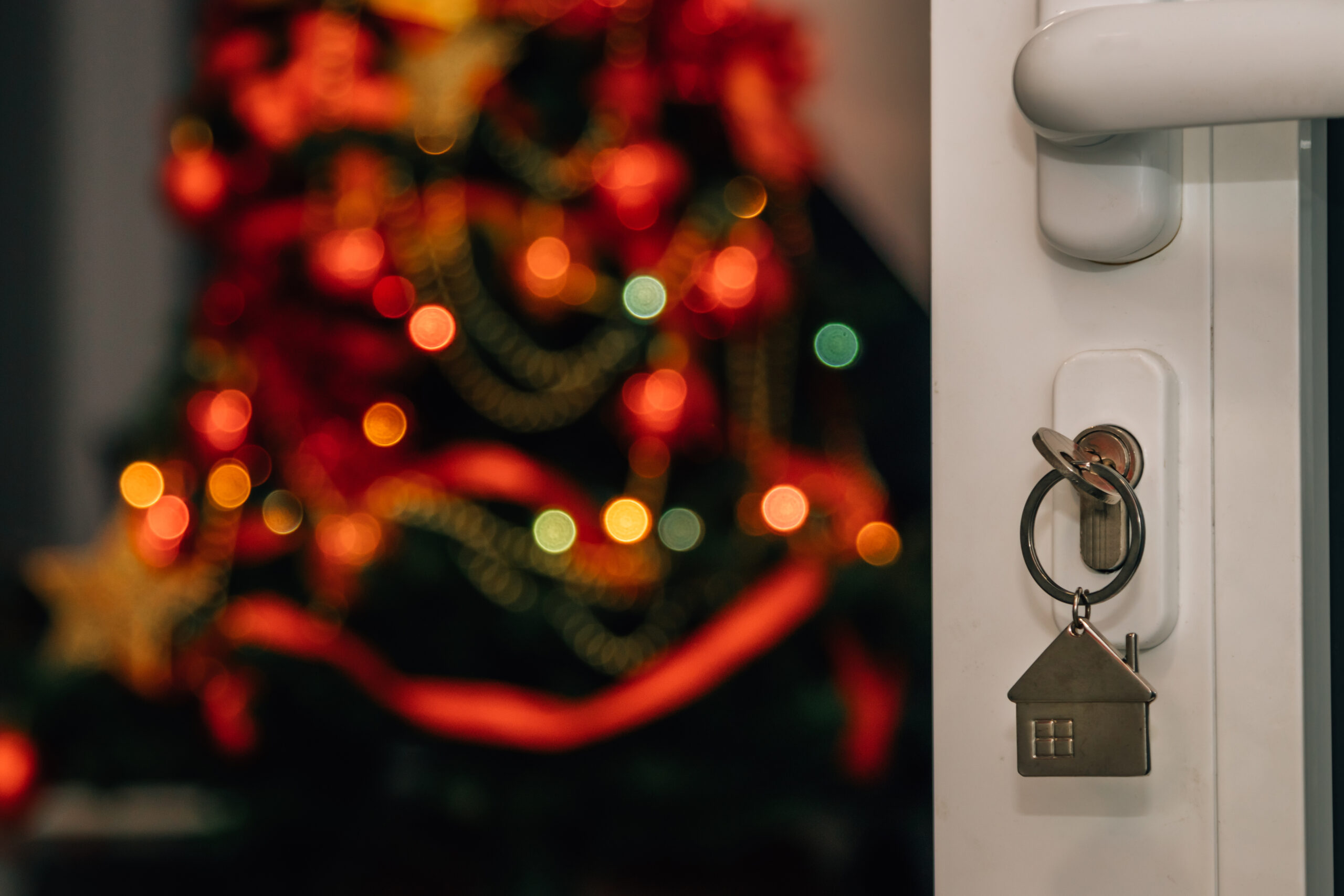 Home door with key inside and Christmas tree with Christmas tree lights in the back