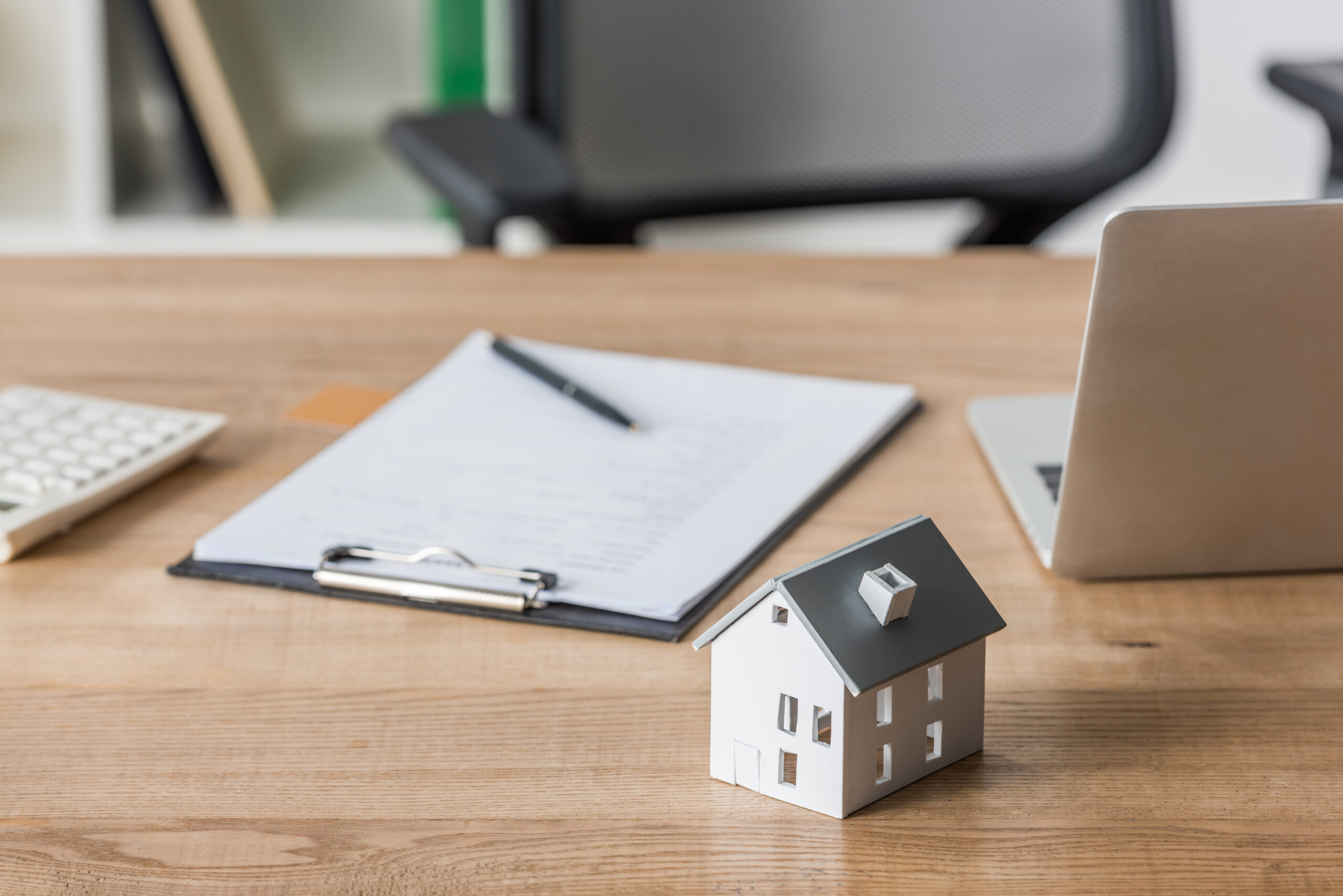 clipboard and laptop near house model on wooden table in office