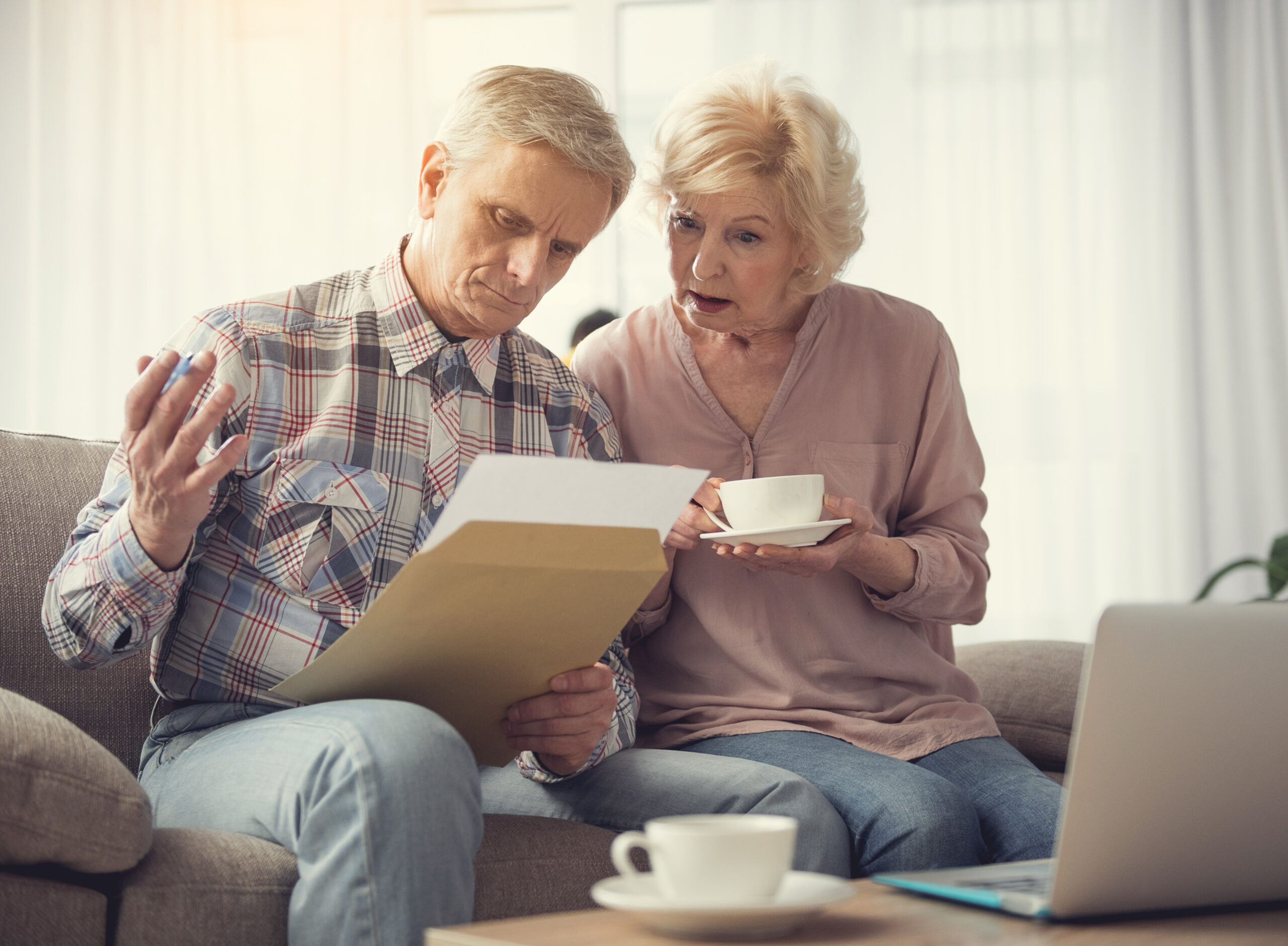 Old couple looking over document with a tea and laptop on sofa