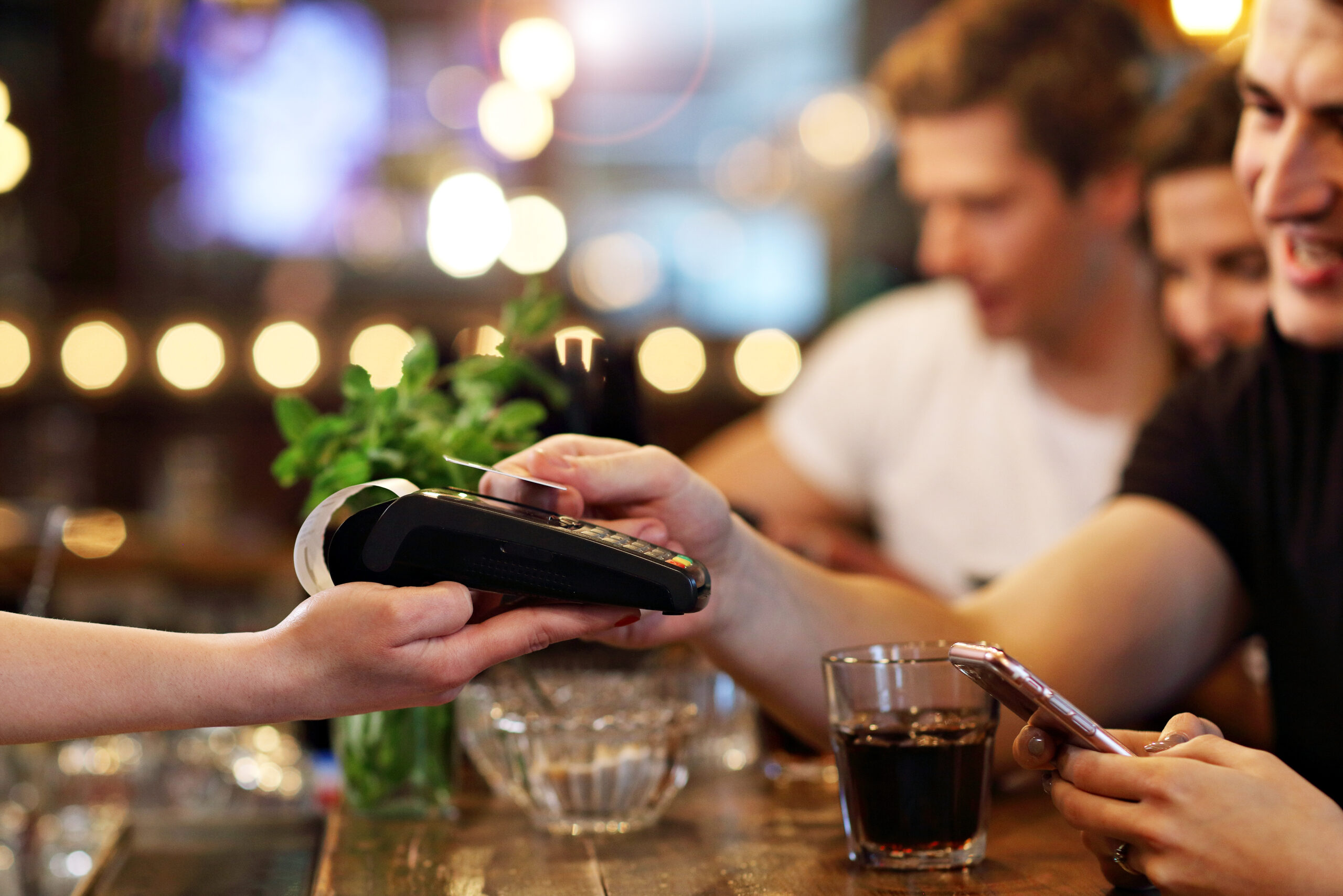 Group Of Young Friends Enjoying Meal In Restaurant. Man paying with card machine