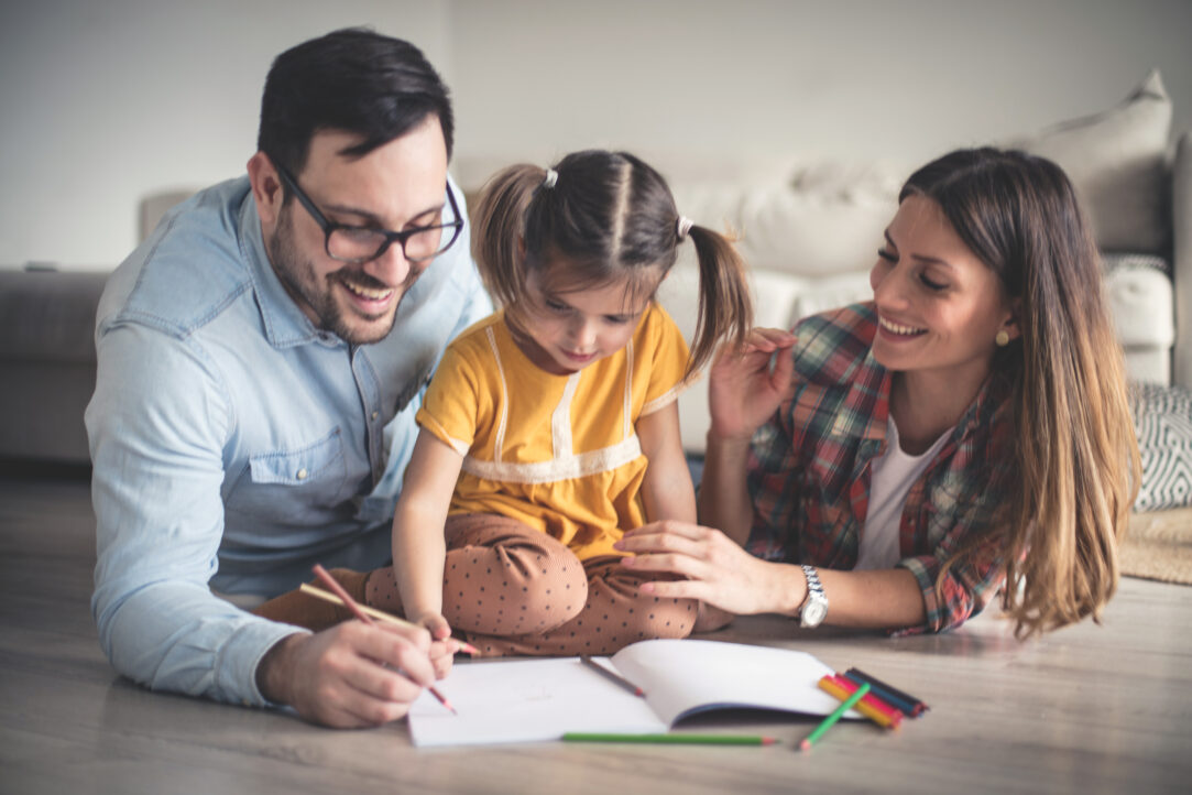 Parents with child helping her colour/ do home work on the floor of living room
