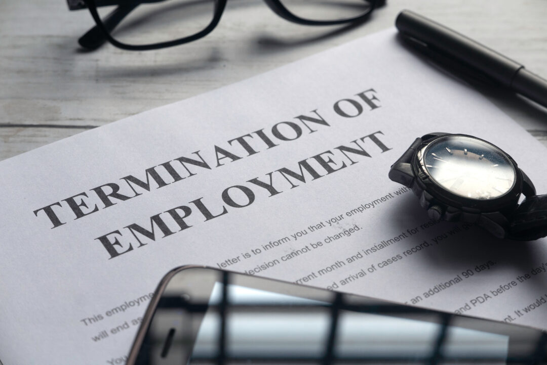 Selective focus of watch,mobile phone,pen,glasses and Termination of Employment letter on a white wooden background.