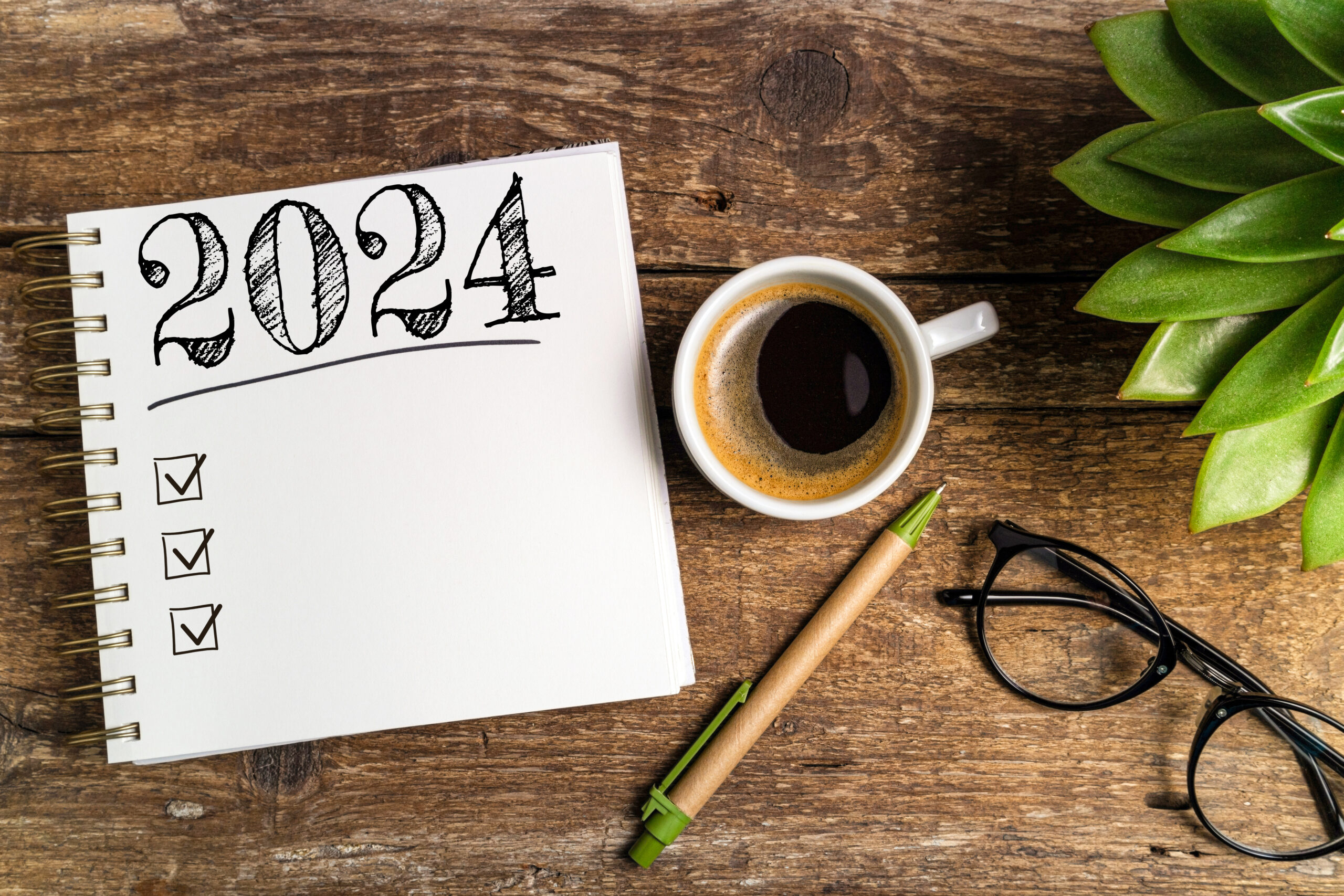 New year goals 2024 on desk. 2024 goals list with notebook, coffee cup, plant on wooden table. Resolutions, plan, goals, action, checklist, idea concept. New Year 2024 template, copy space