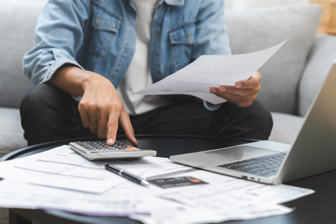 Business financial concept, young man, male sitting on couch stressed hand calculate expense on table at home from invoice or bill have no money to pay mortgage or loan, debt bankruptcy.