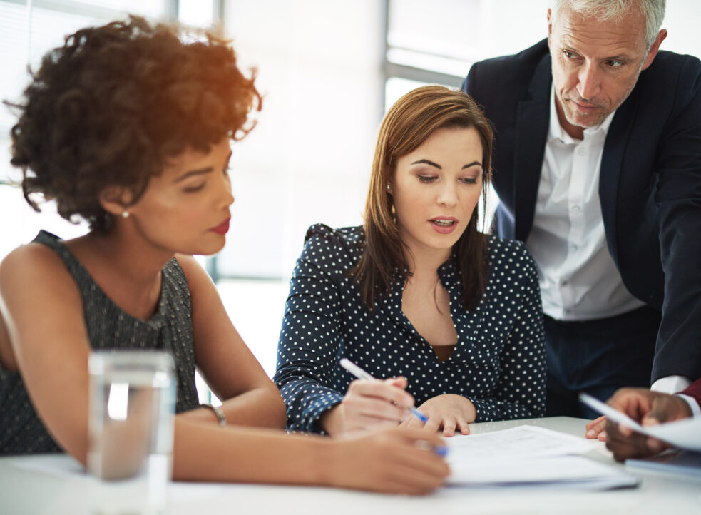 three people in corporate meeting, thinking and reading over a document and paperwork