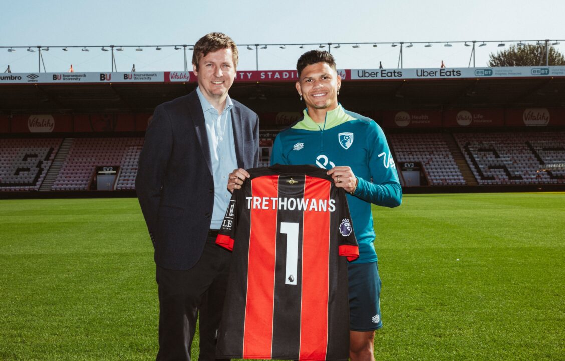 Darren Lovegrove standing with Bournemouth FC player holding up Trethowans football top on football pitch