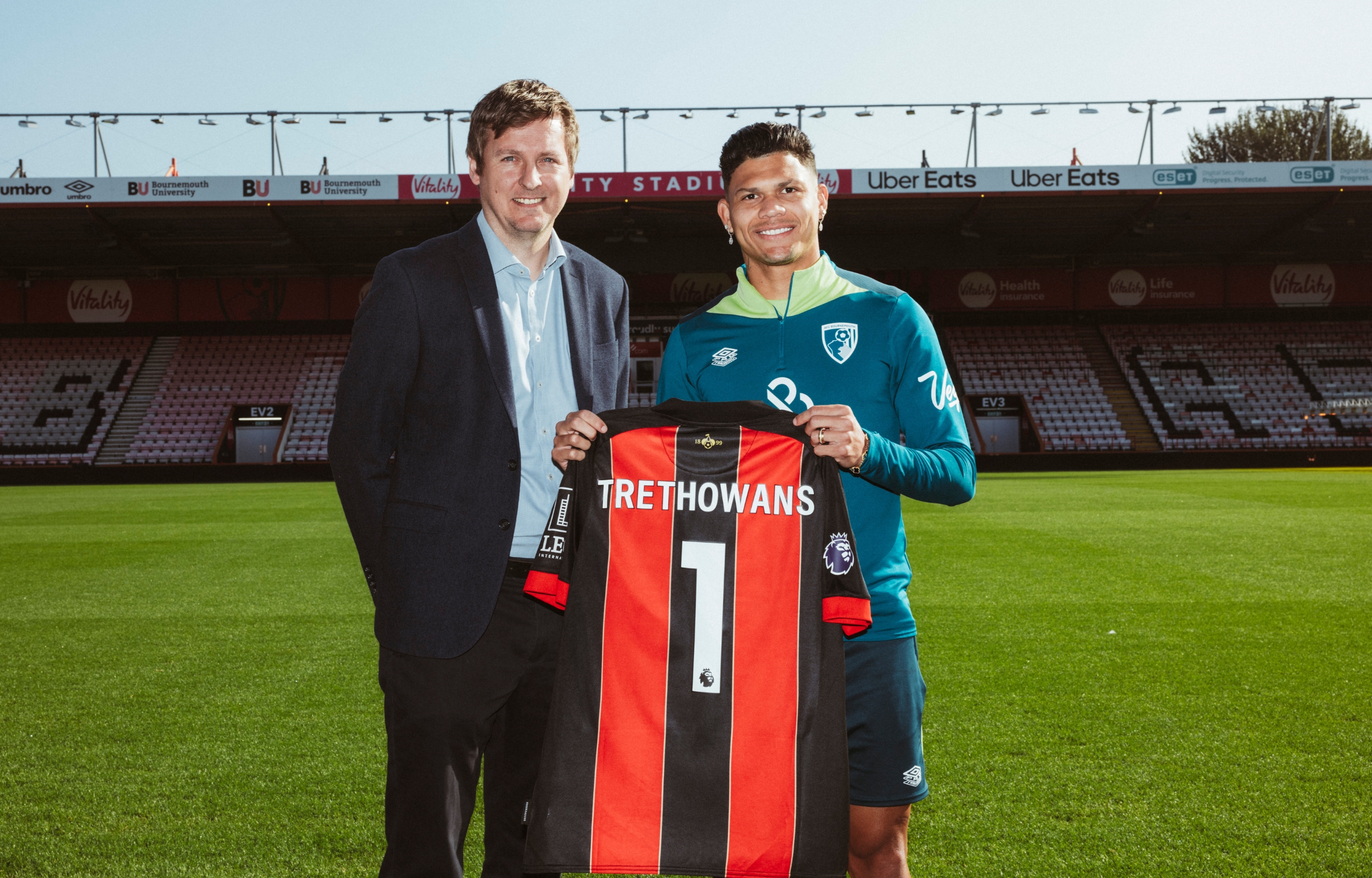 Darren Lovegrove standing with Bournemouth FC player holding up Trethowans football top on football pitch