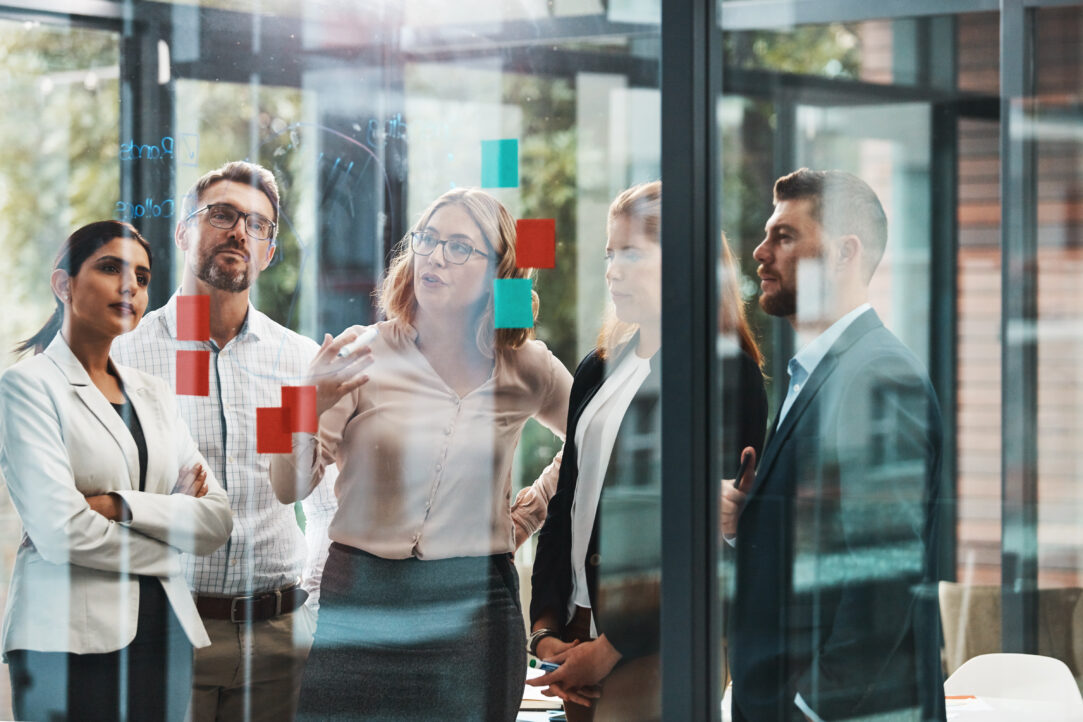 Woman, group and discussion with notes on board with review, listening and planning with brainstorming. Coach, training and team by glass wall, questions and collaboration with strategy in office.
