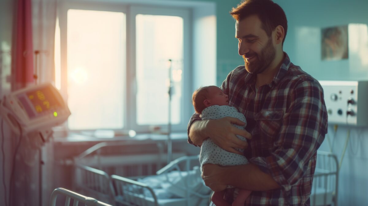 a photo of a man holding a newborn baby on a hospital ward